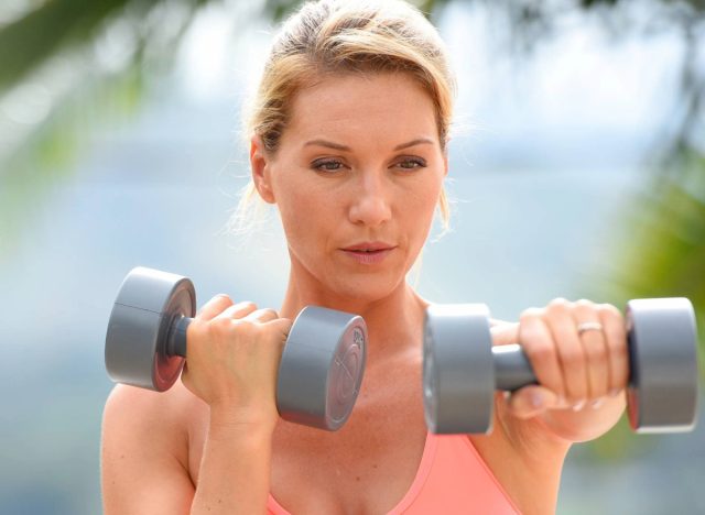 middle aged woman doing dumbbell exercise outdoors, concept of body weight training to regain muscle mass