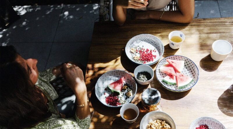 Two people eating lunch outside with plates of watermelon, pomegranates, and various seeds and nuts